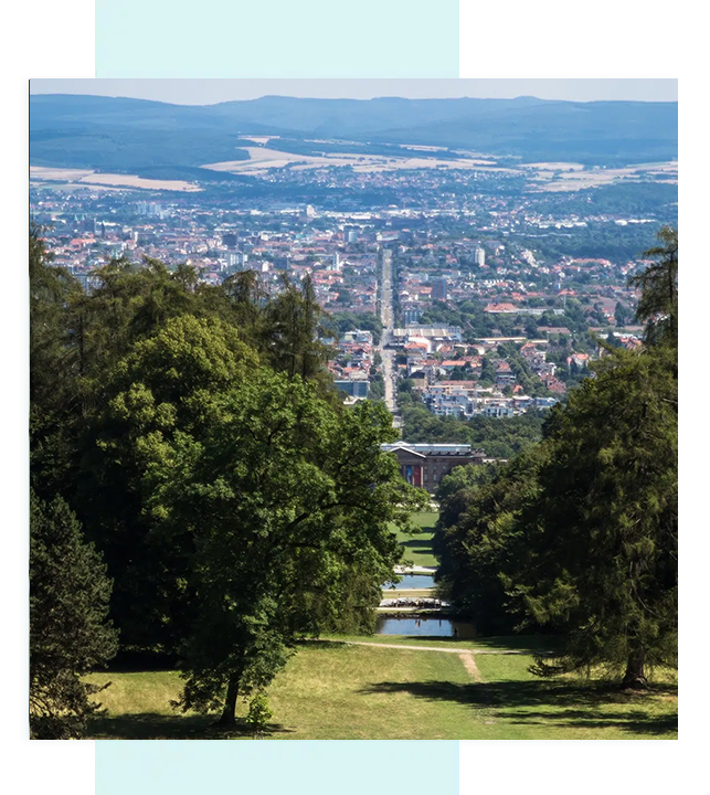 Stadtpanorama mit Bäumen im Vordergrund, Hügel im Hintergrund.